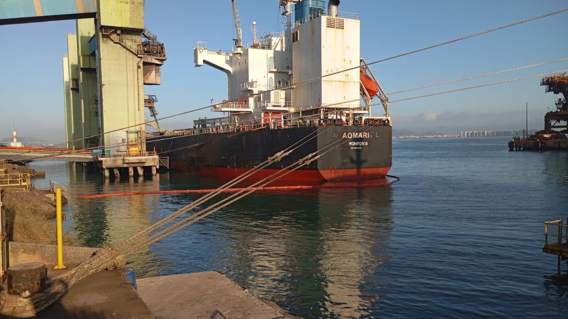 Navio atracado com barreira de contenção instalada na água durante resposta ambiental